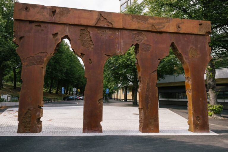 A large, gate-like sculpture placed in an urban space.