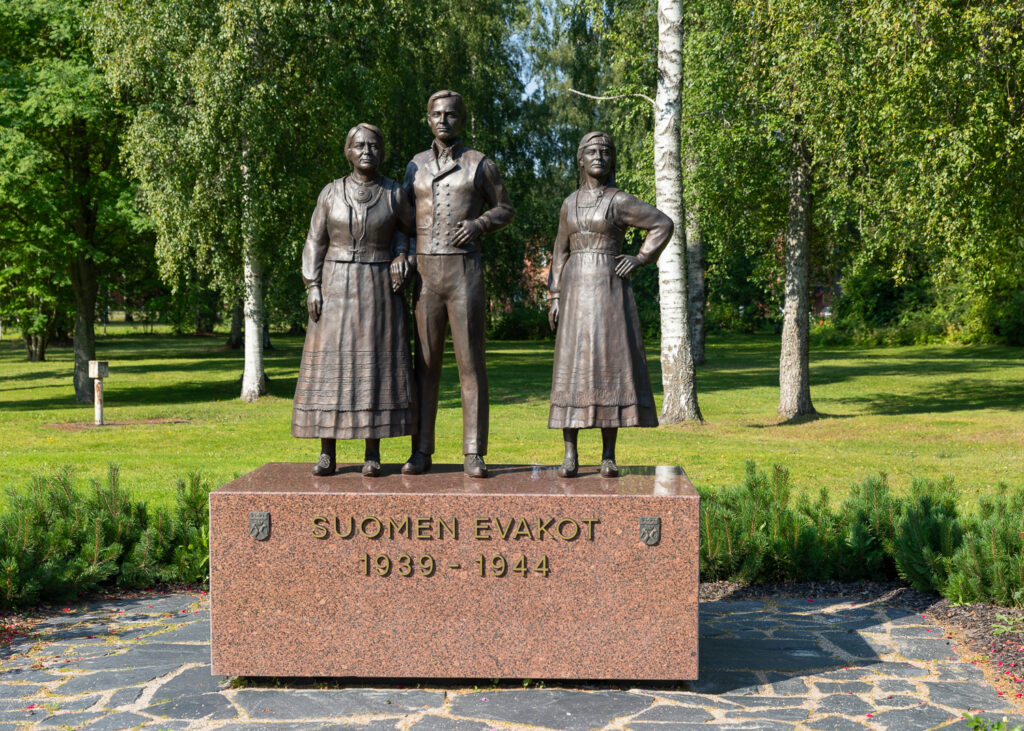 Kolmen pronssisen ihmishahmon patsas neliskanttisen graniittisen jalustan päällä.